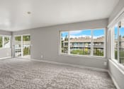 Thumbnail 3 of 8 - A spacious room with grey carpeting and large windows overlooking a residential area.